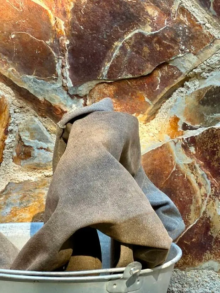 Do You See The Back Of A Man Wearing A Long Cloak With A Hood, Trying To Climb Out Of The Bucket?