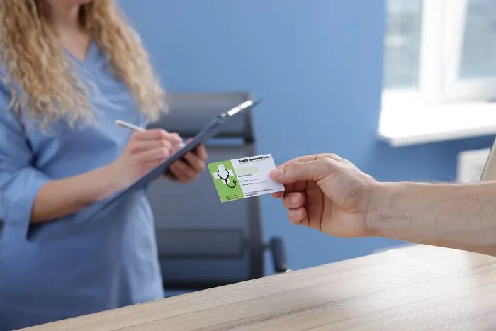 A patient hands a health insurance card to a nurse, who is writing on a clipboard, highlighting patient care in emergencies.