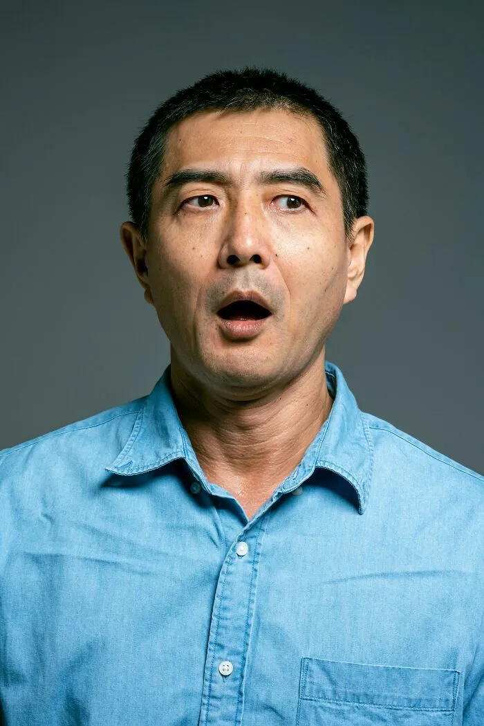 A man in a blue shirt with a shocked expression, mouth open, looking wide-eyed. Illustrates family secrets.