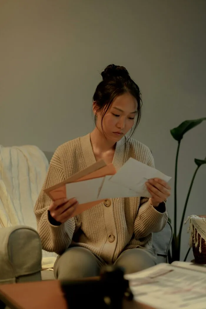 A young woman intently examining papers and envelopes, possibly discovering family secrets or shocking news.