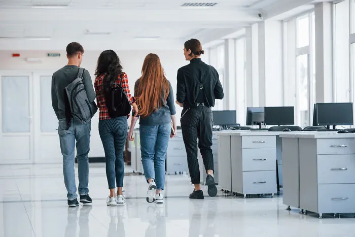 Students walk through a modern office, symbolizing absurd rules in schools and workplaces.