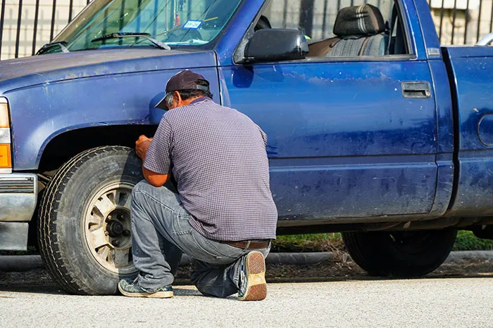Man checking tire of blue pickup truck outdoors demonstrating safety tips everyone should know for vehicle maintenance.