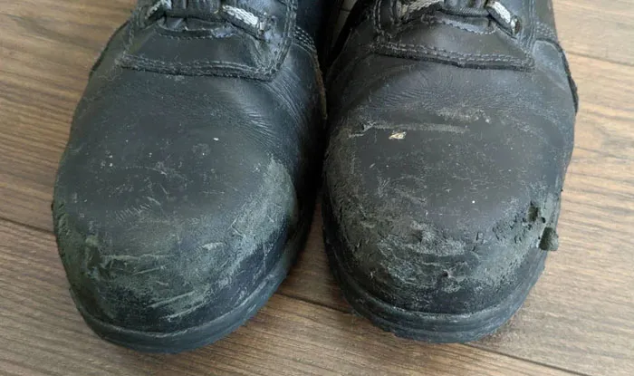 Worn-out black safety boots showing heavy damage, highlighting the importance of proper safety tips for protection.