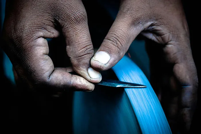 Close-up of hands carefully sharpening a blade on a grinding wheel emphasizing safety tips for handling tools.
