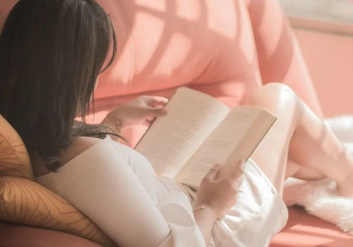 Woman reading a book on a sofa, demonstrating intelligence. Her focus suggests a mind almost artificial in its depth.