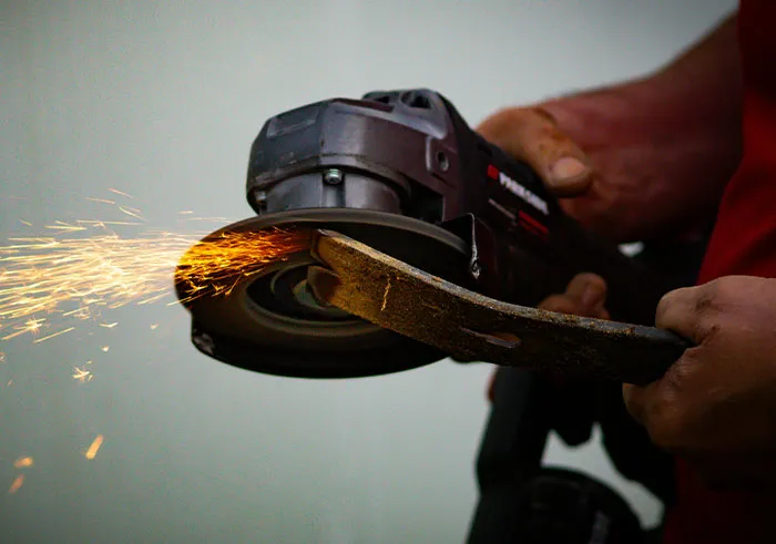 Hands operate an angle grinder on metal, generating bright sparks. Reflects a mind where intelligence seemed almost artificial.