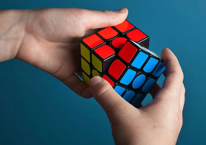 Hands solving a colorful Rubik's cube against a blue background, a classic test of intelligence.