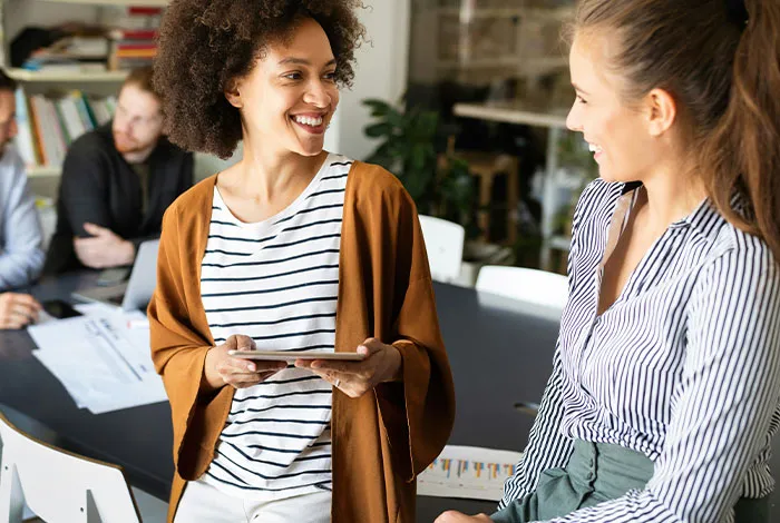 Two women smiling, discussing ideas in an office. Their intelligence seems almost artificial.