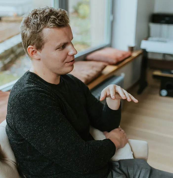 Man in a black sweater gesturing thoughtfully indoors, illustrating subtle and interesting displays of intelligence.