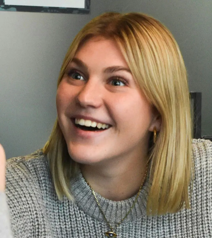 Young woman with blonde hair smiling, showing subtle and interesting displays of intelligence in a casual setting.