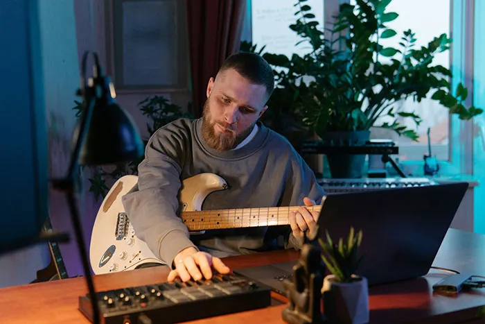 Man playing electric guitar and using music equipment at desk with laptop, showcasing subtle and interesting displays of intelligence.
