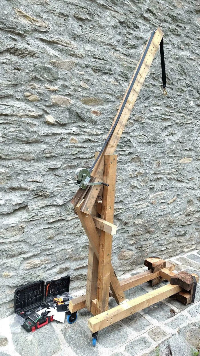 A DIY wooden crane used as a clever solution for lifting, standing against a stone wall with tools nearby.