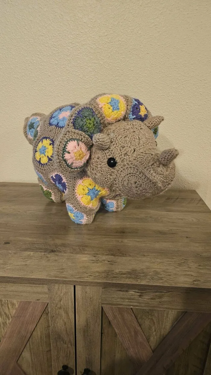 Crocheted multicolor dinosaur amigurumi stuffed toy on wooden table