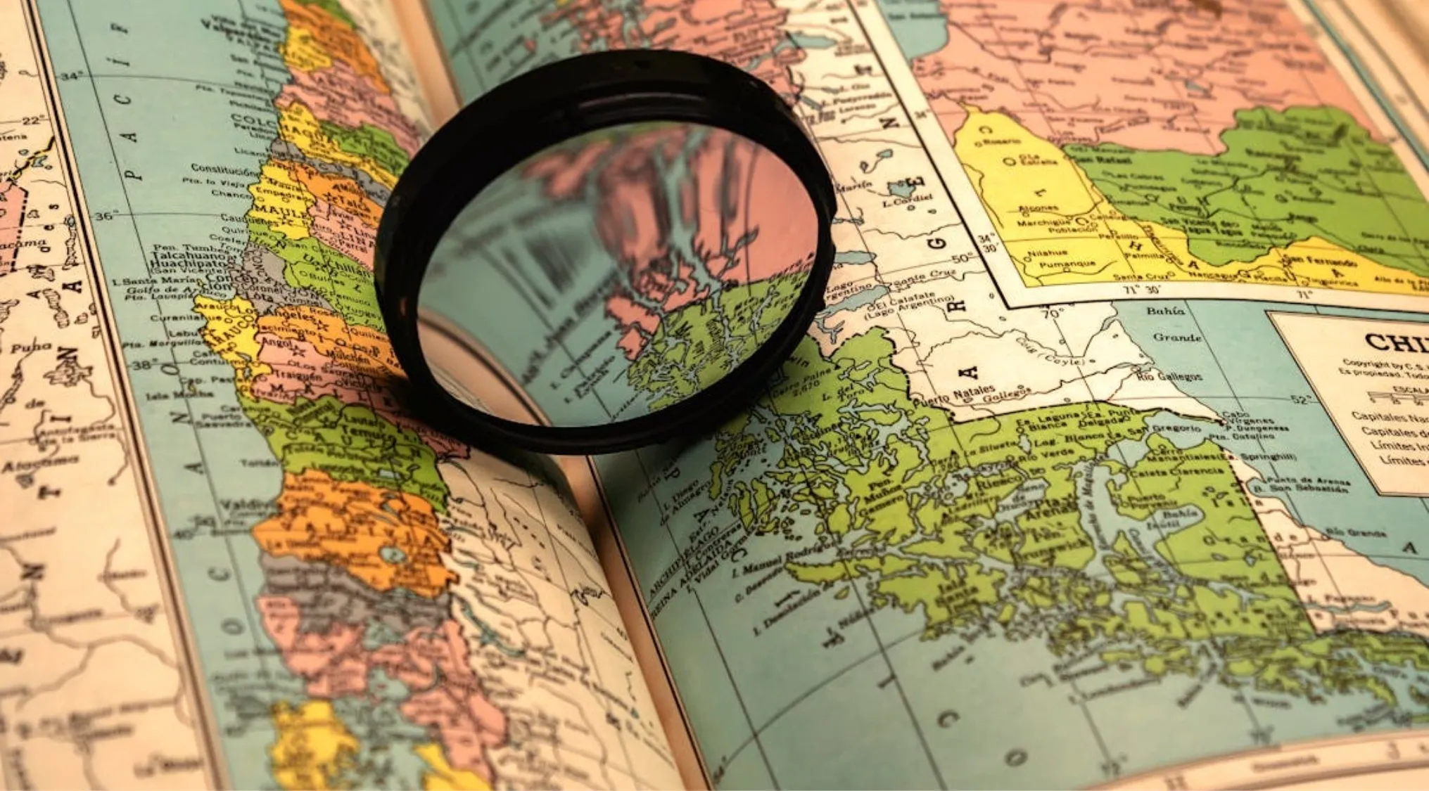 A magnifying glass on a vintage map, focusing on the countries in South America and potential dependent territories.