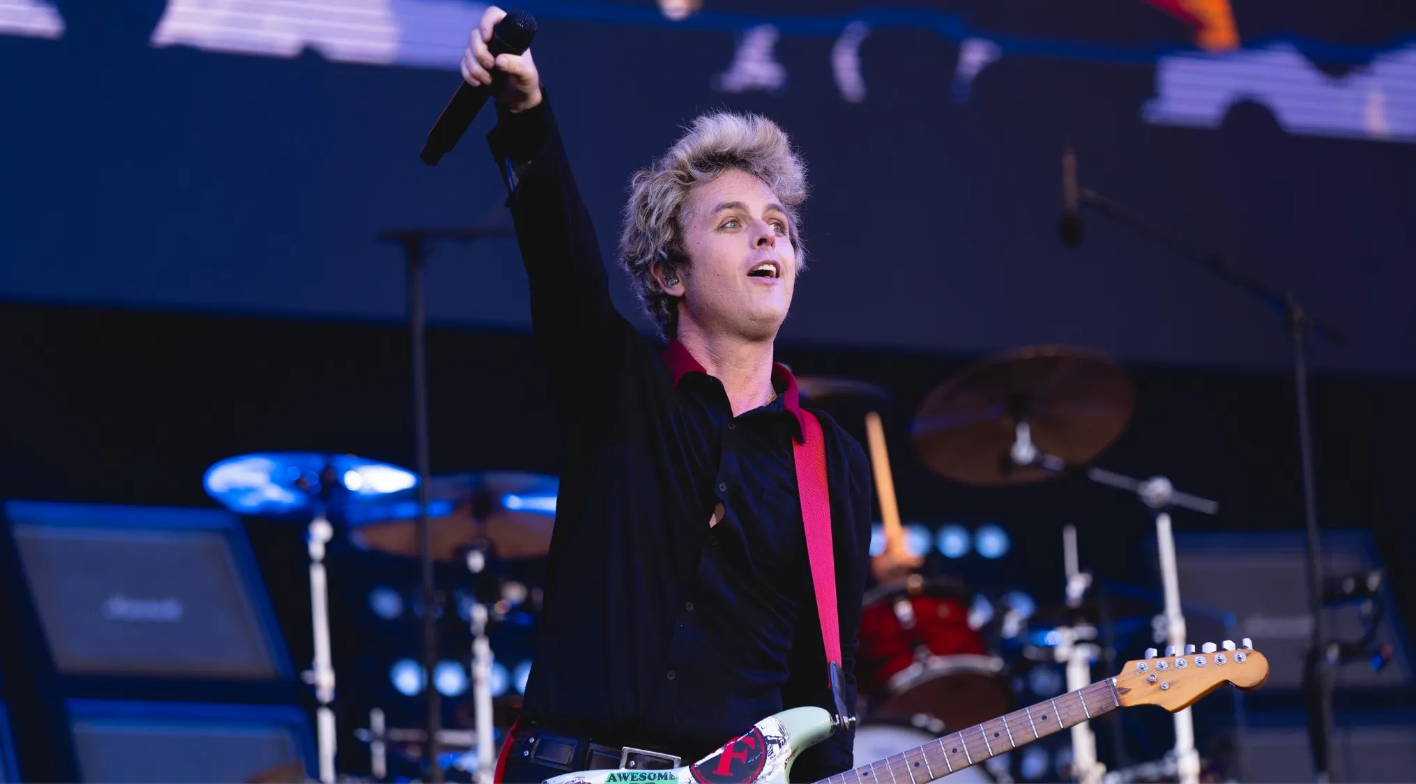 Billie Joe Armstrong performing live, holding a microphone with his electric guitar. Music challenge: Name 30 bands.