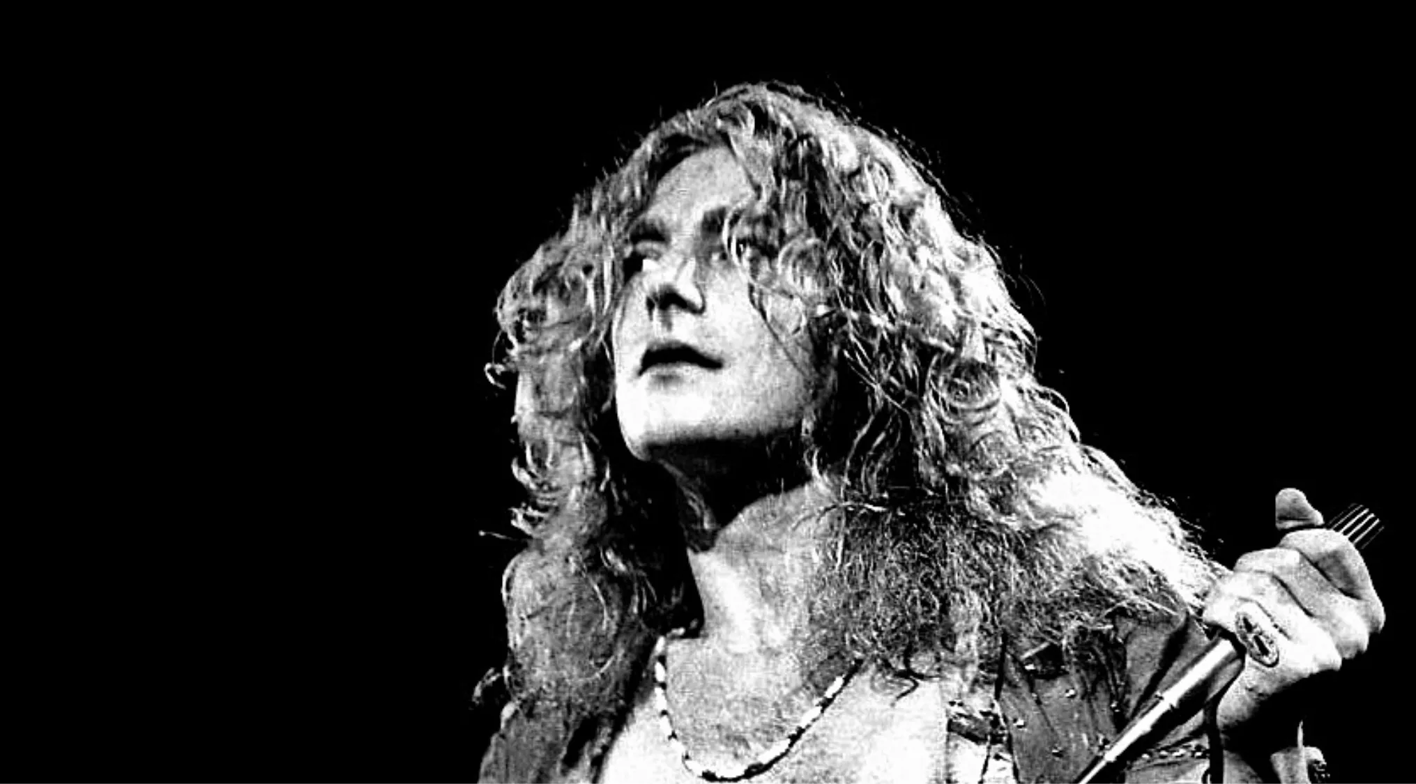 Black and white photo of a lead singer with long curly hair, holding a microphone. Music Challenge. '80s band.