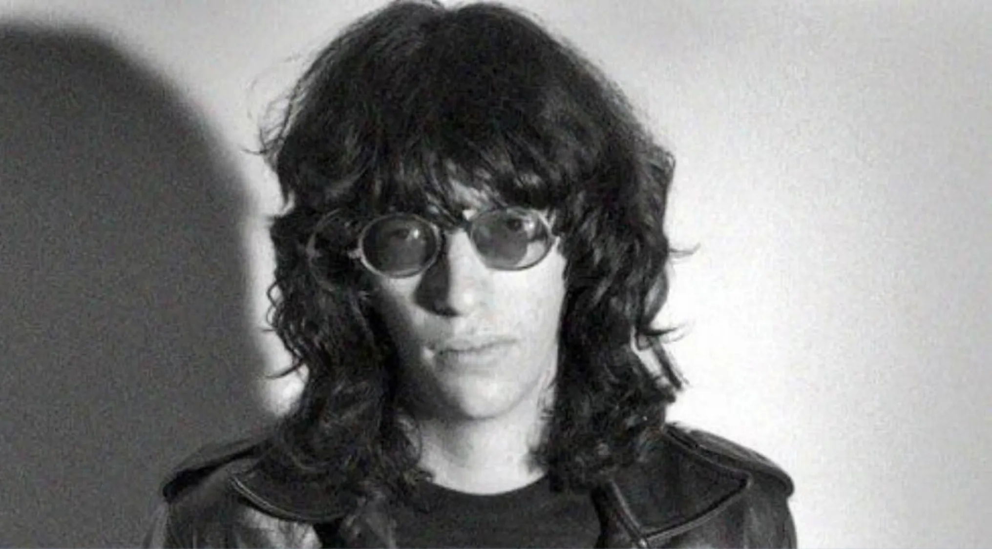 Black and white photo of a lead singer with long hair and round sunglasses for the Music Challenge. Name 30 Bands.
