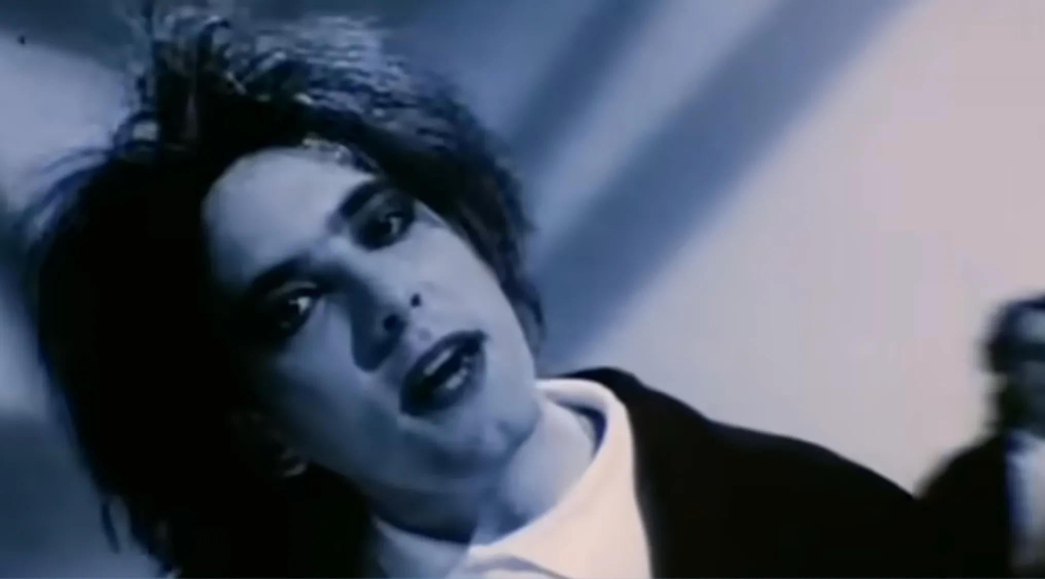 Close-up of a Lead Singer with dark, messy hair and heavy eye makeup, looking directly at the camera. Music Challenge.