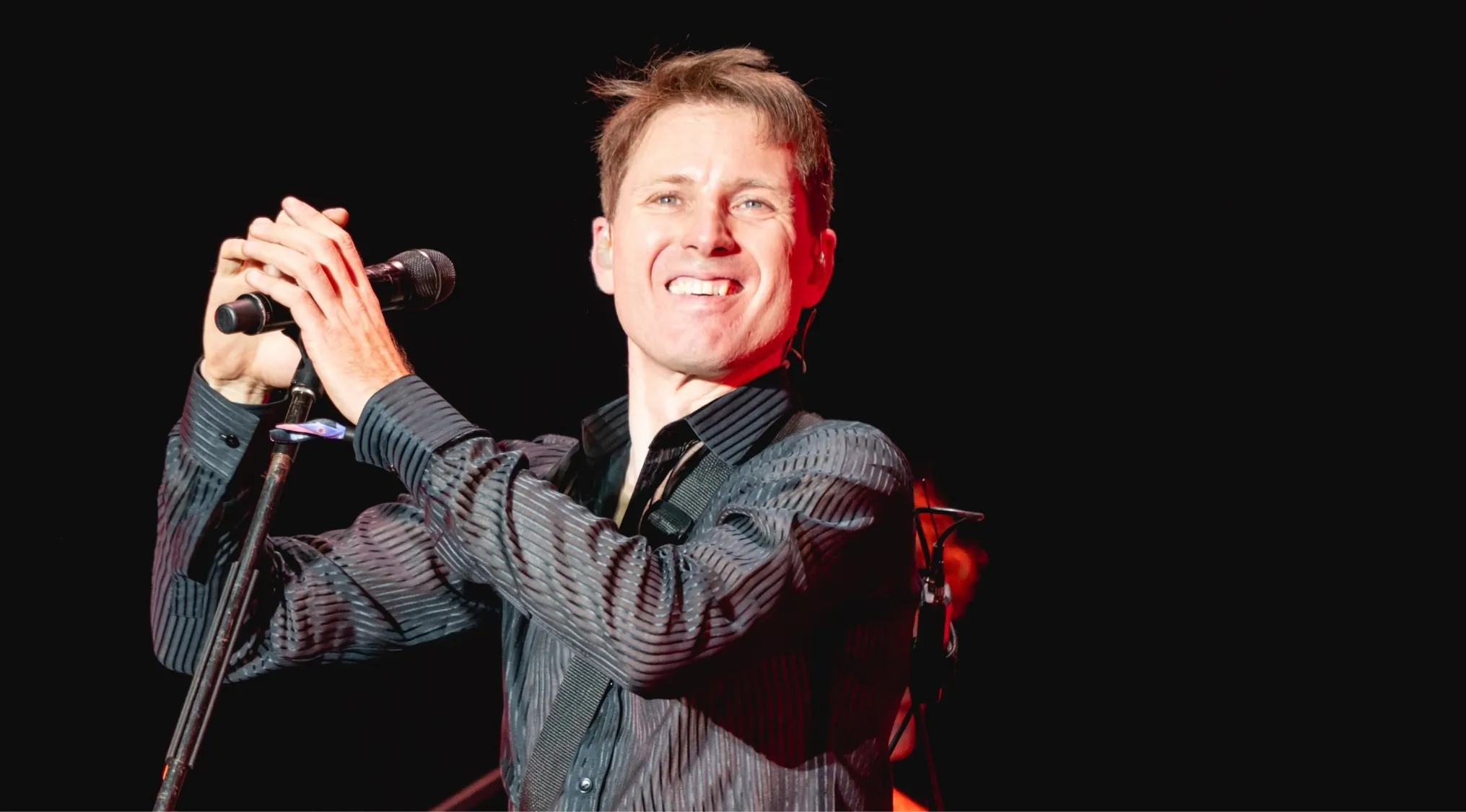 Lead singer smiling, holding a microphone. Link the frontman to the band and name 30 bands.