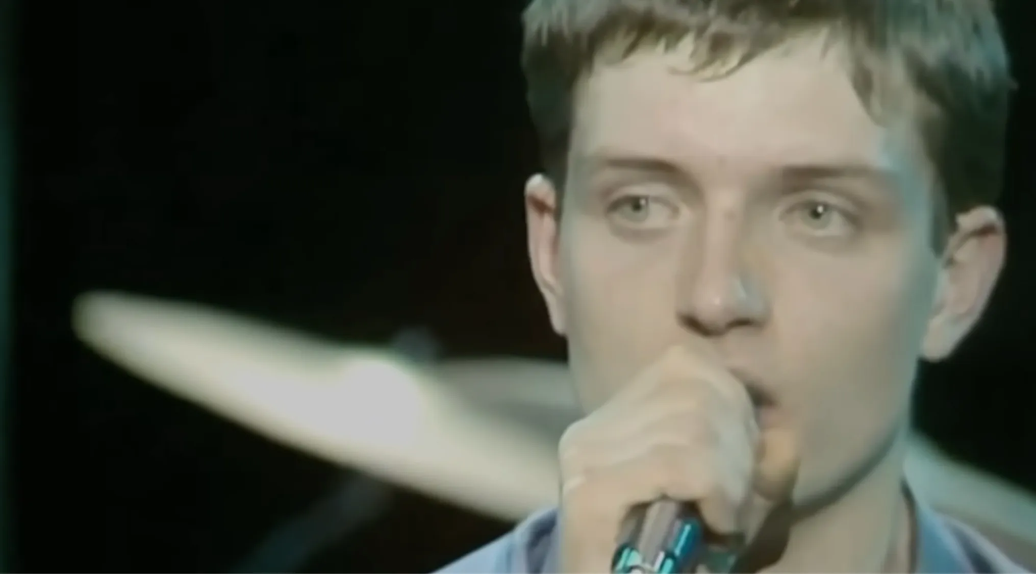 Ian Curtis, the frontman of Joy Division, singing into a microphone, focused expression. Music challenge: Name 30 bands.