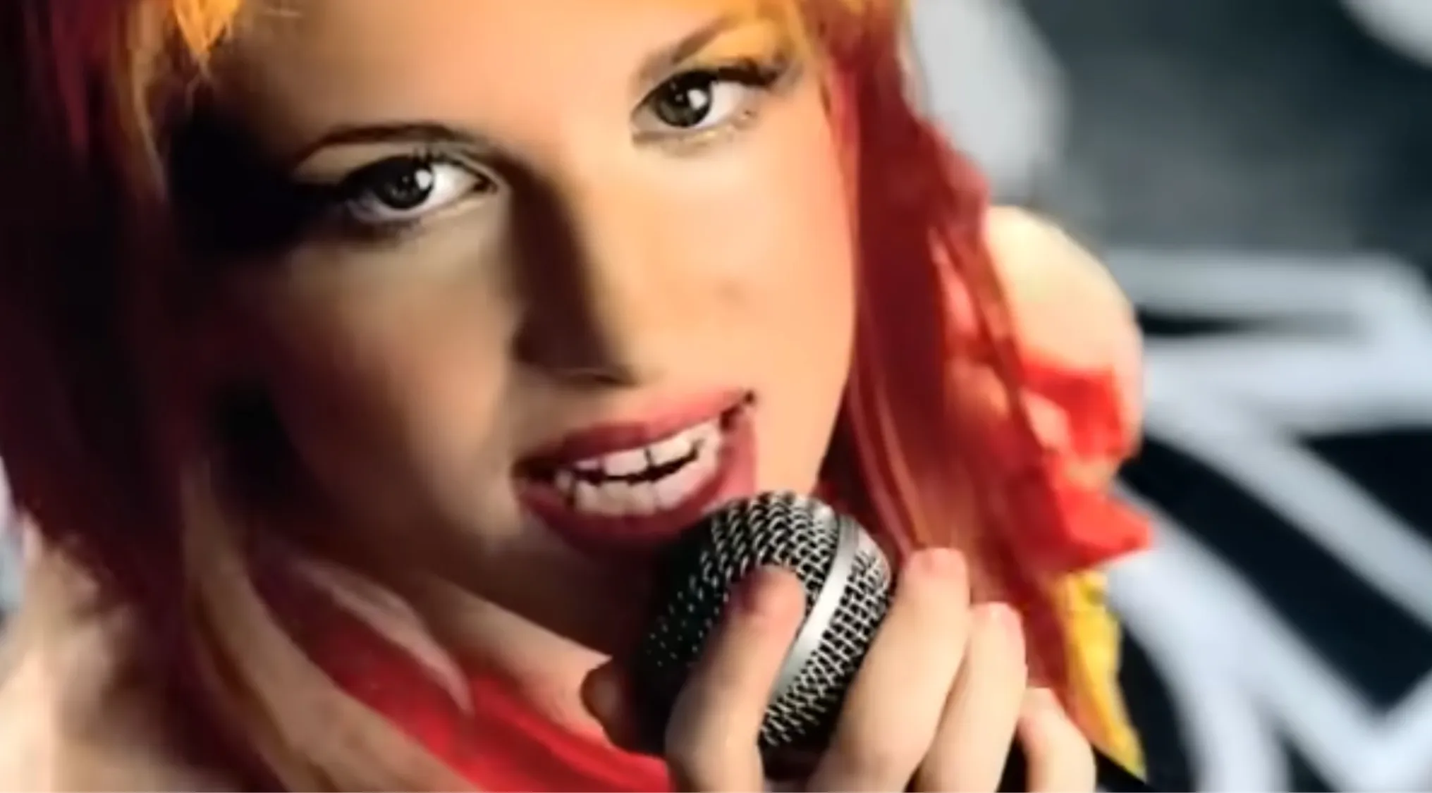 Hayley Williams singing into a microphone, her red and orange hair vibrant against a dark background. Music Challenge.