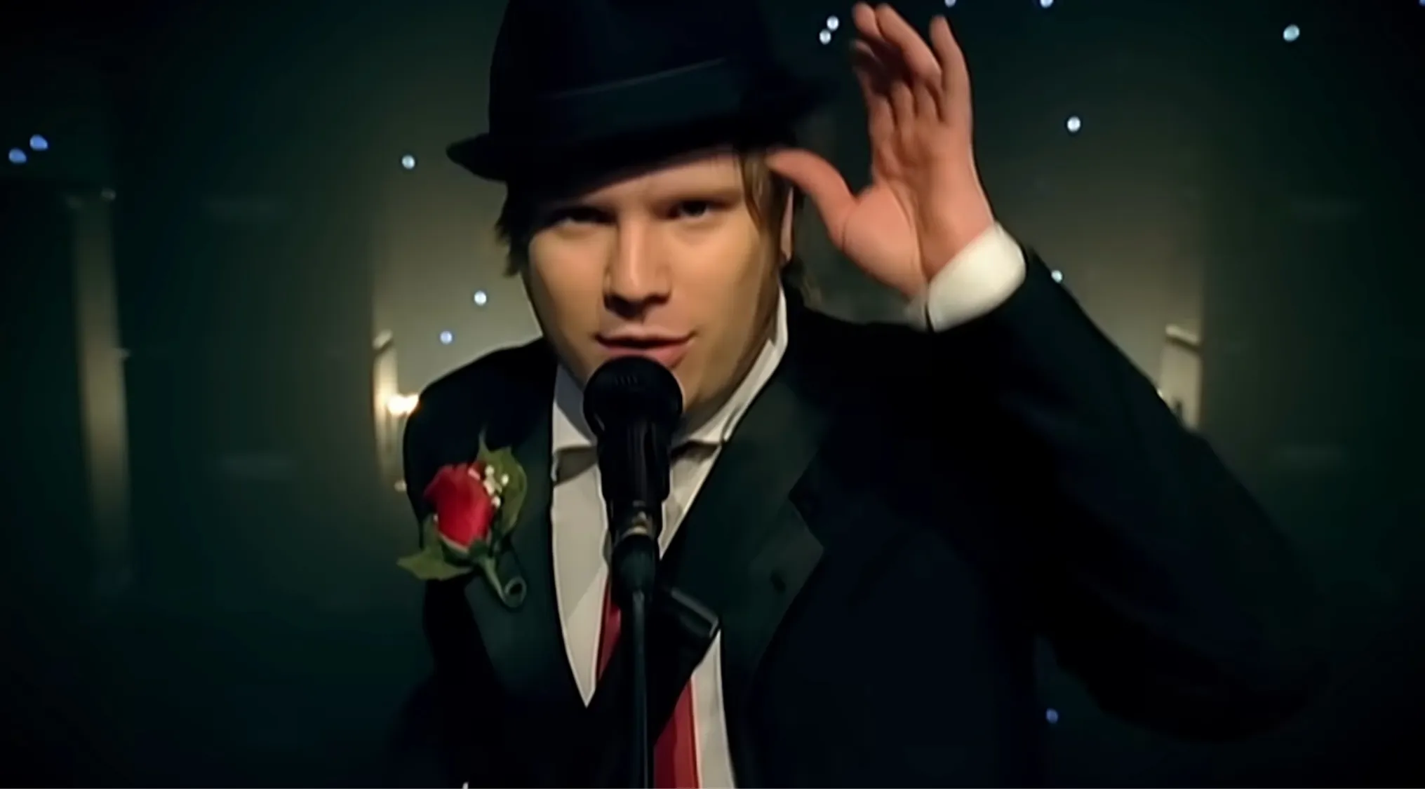 Patrick Stump, lead singer of Fall Out Boy, in a black fedora and tuxedo with a red boutonniere, singing into a mic. Music Challenge: Name 30 Bands.