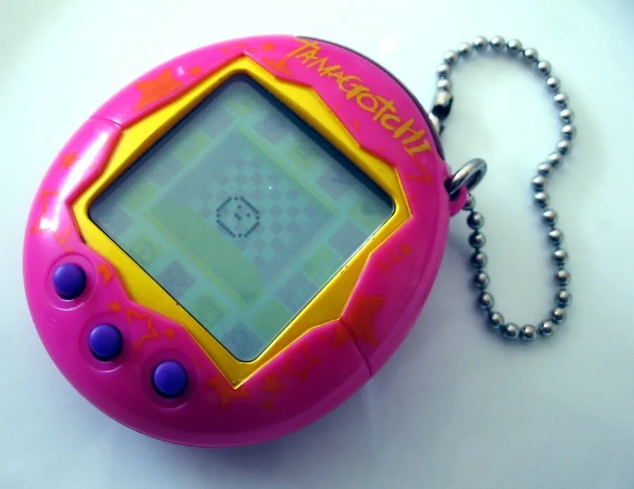A pink Tamagotchi, a retro gadget, with a yellow border around its screen and purple buttons, featuring a chain.