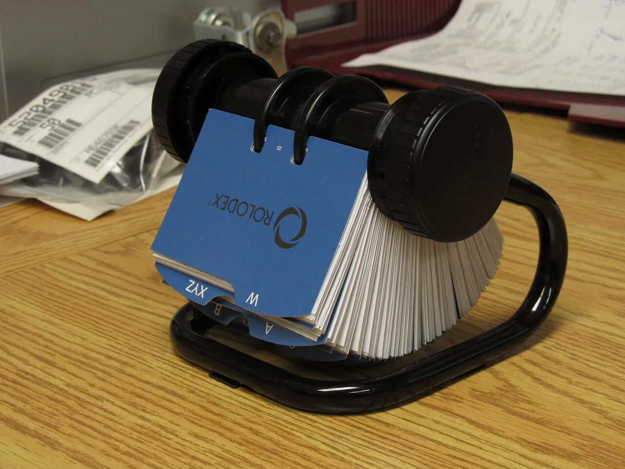 A black Rolodex with blue index cards on a light wooden desk, a retro gadget for organization.