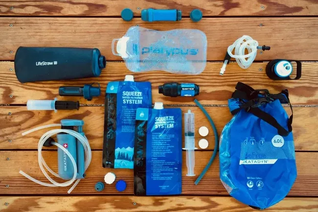 Various water purification kit items like filters, bladders, and squeezable pouches laid out on a wooden surface.