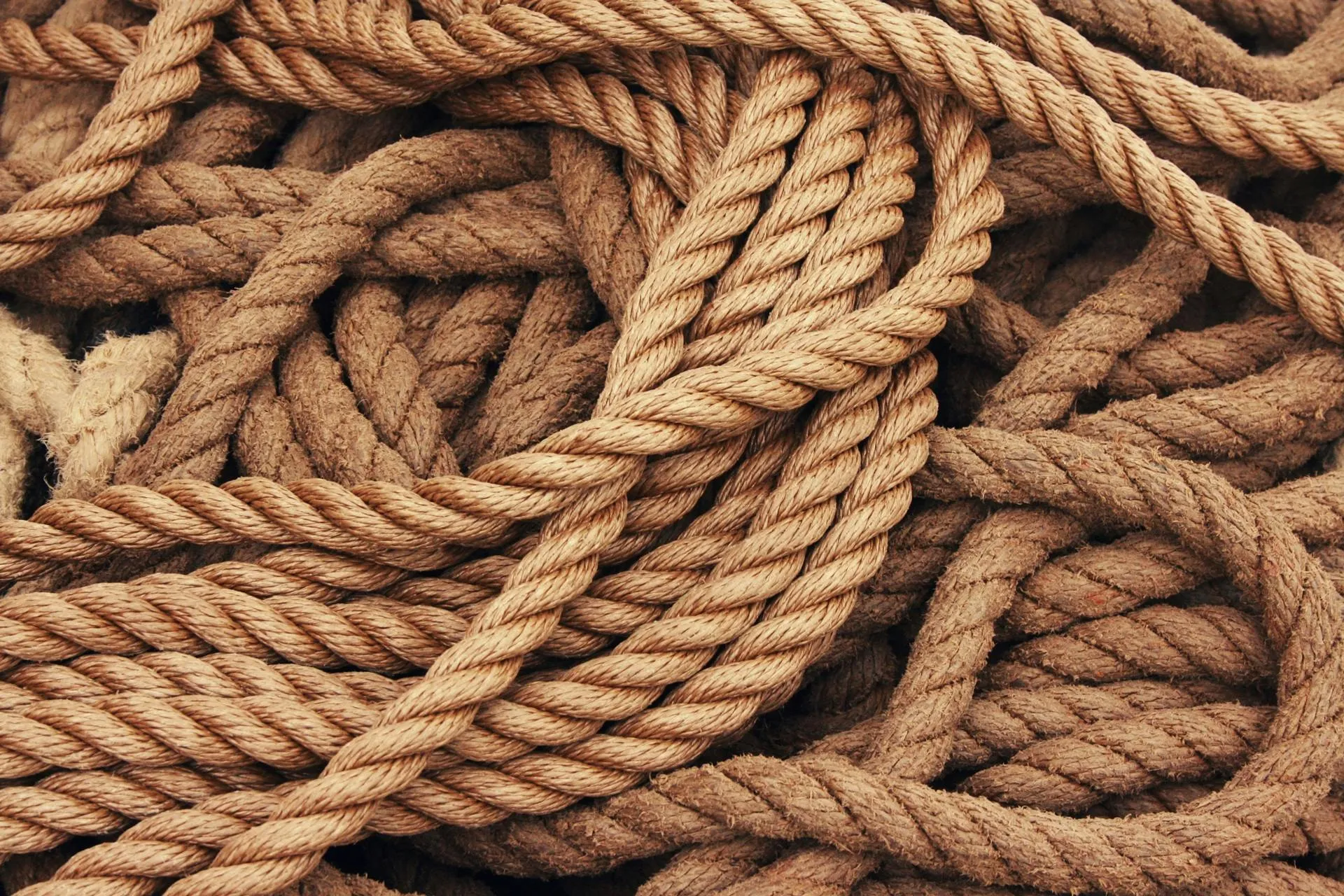 Close-up of a tangled pile of light brown, natural fiber rope. A single strand of rope is visible.