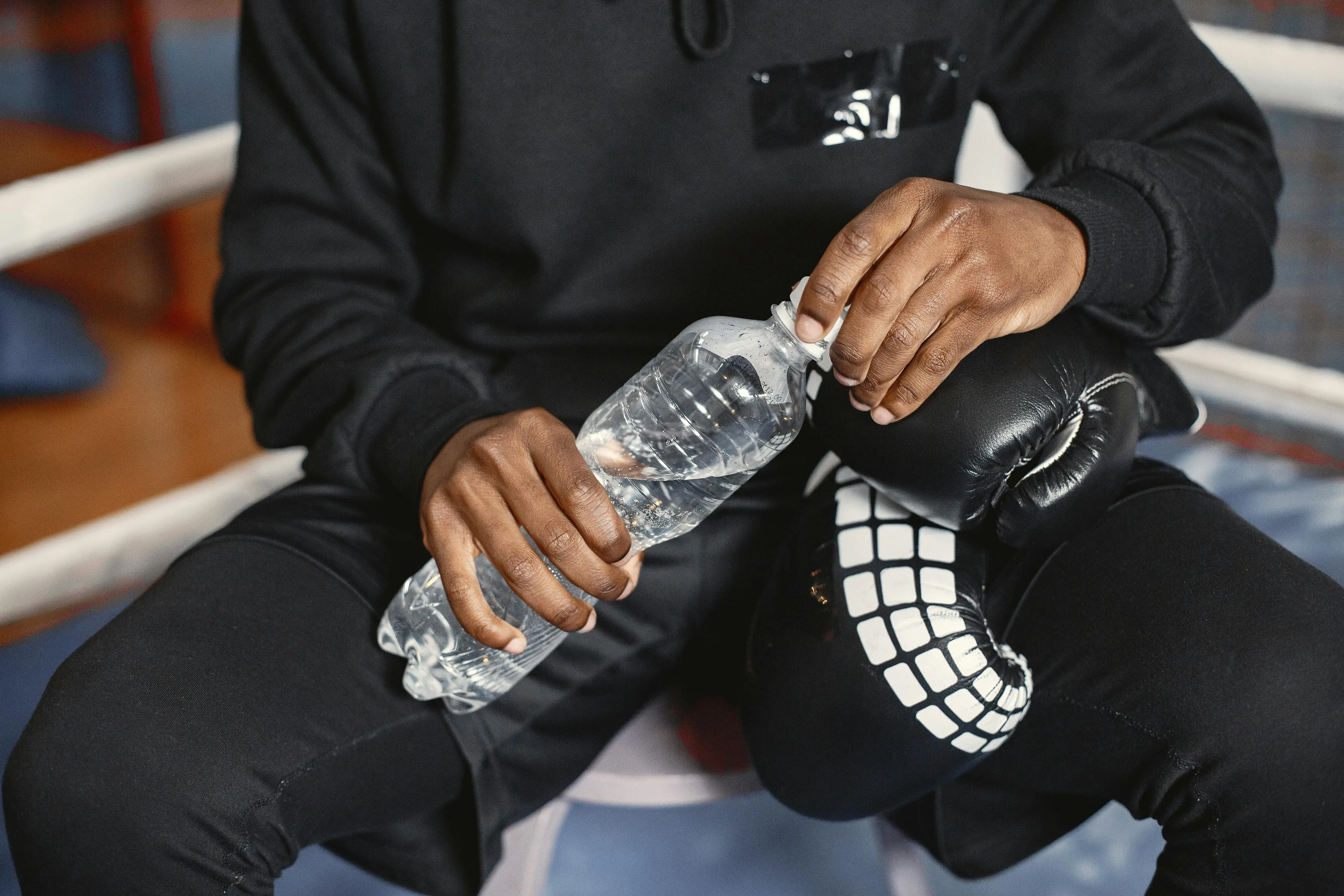 A boxer in black attire, holding a bottle of water and resting, possibly after training. Deserted island survival.