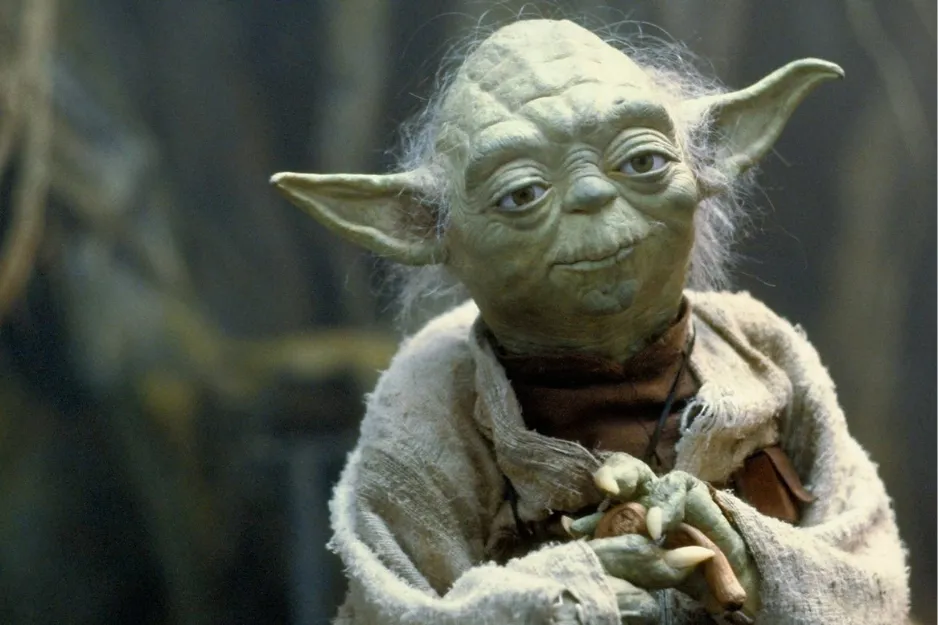Yoda, the wise fictional mentor, smiling and holding a small stick, in his iconic robes.