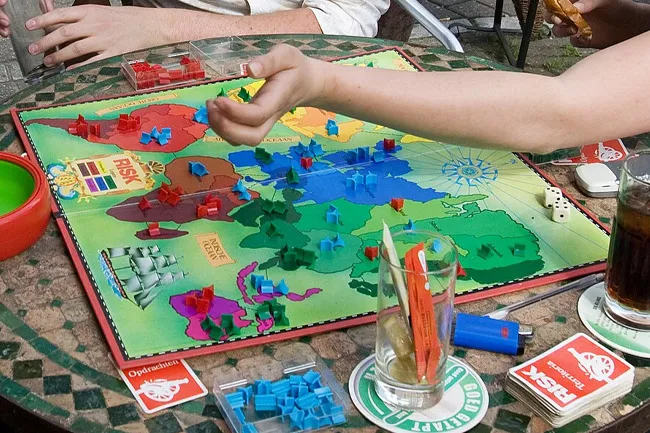 Friends playing Risk, a classic board game, during game night, with pieces on the board and dice nearby.