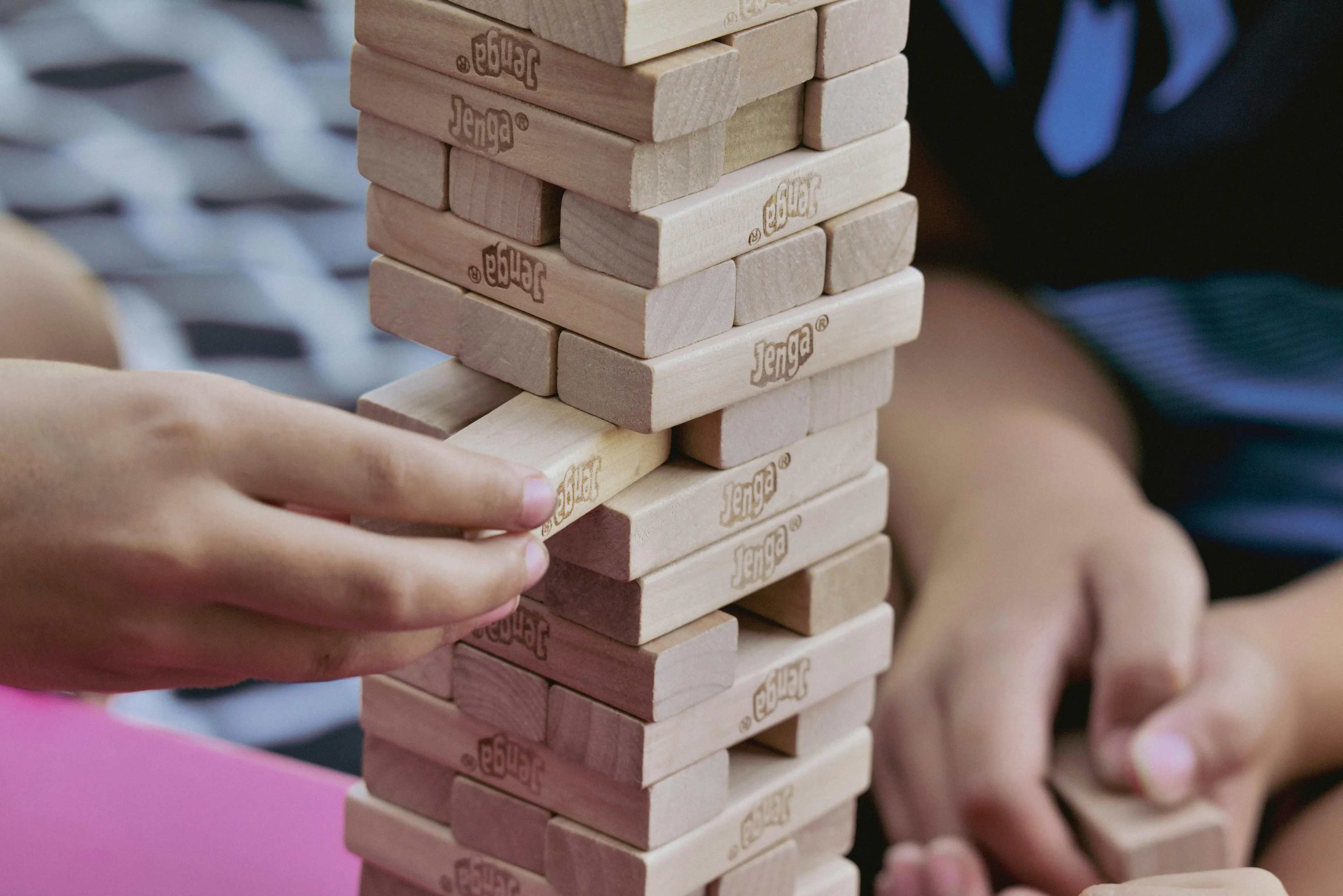Hands carefully pulling a block from a Jenga tower during a classic board game night. Perfect for family fun.
