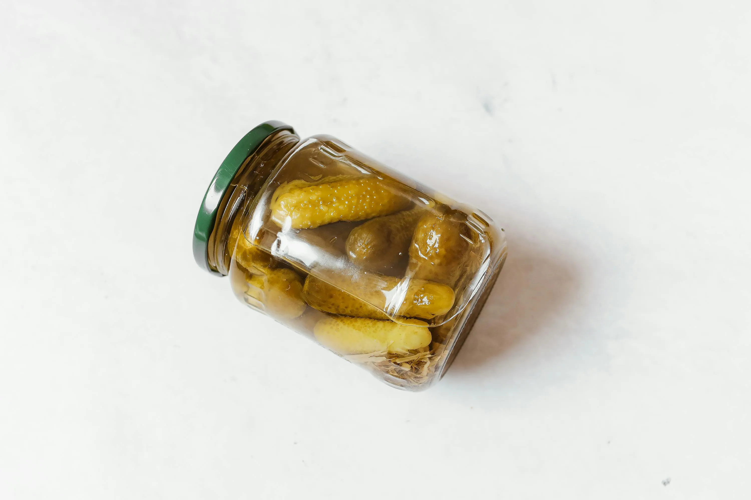 A clear glass jar of pickles, tilted on a white background, suggesting a perfect late-night snack option.