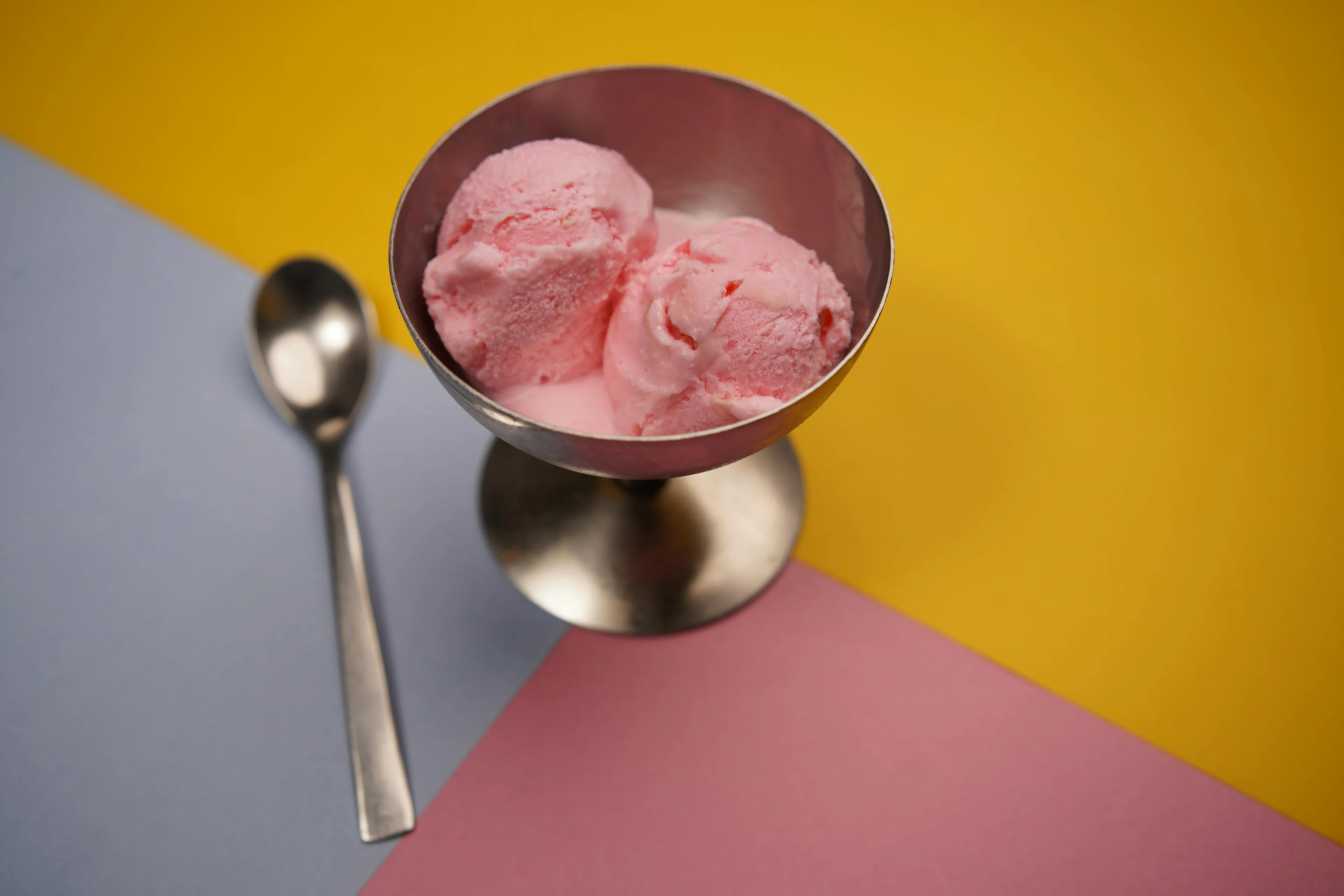 Pink ice cream scoops in a metal bowl with a spoon on a colorful background, perfect for a late-night snack.