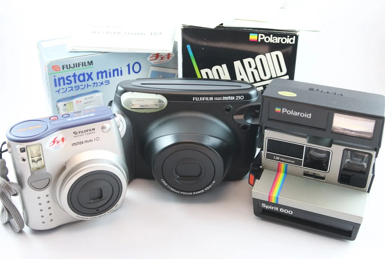 Three retro Polaroid cameras, including Fujifilm Instax models, with boxes in a white background.