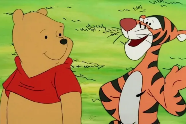 Winnie the Pooh in a red shirt, looking at a joyful Tigger with an open mouth and raised arm.