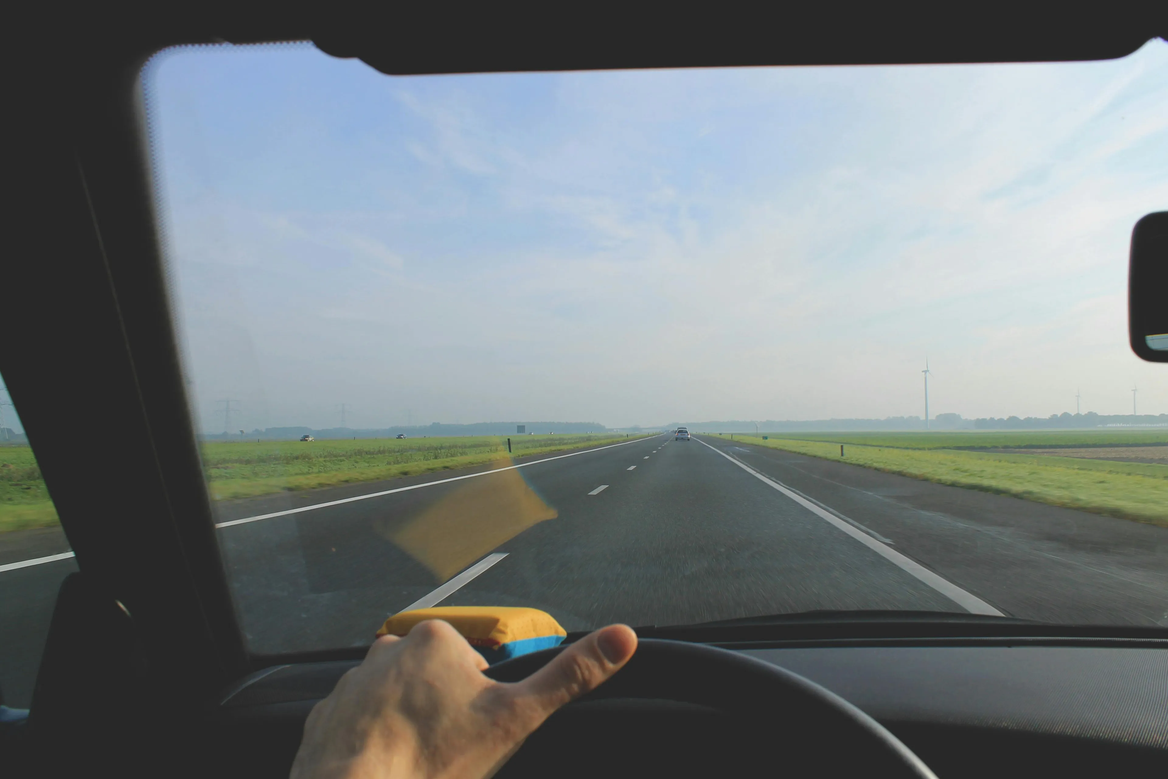 A solo road trip view from the driver's seat on a summer day, driving on a highway through green fields.
