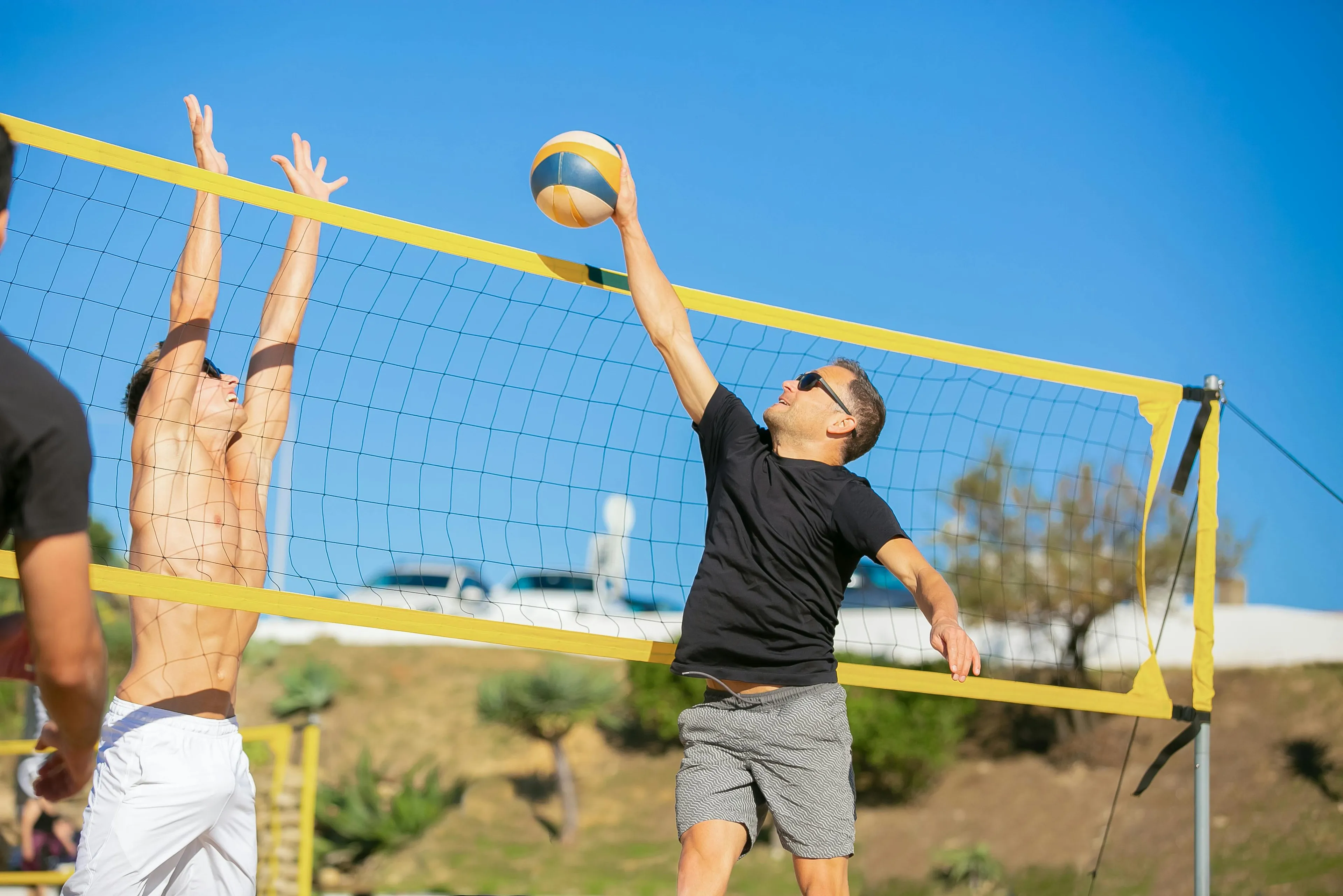 Two men playing beach volleyball on a sunny summer day. One player spikes the ball over the net.