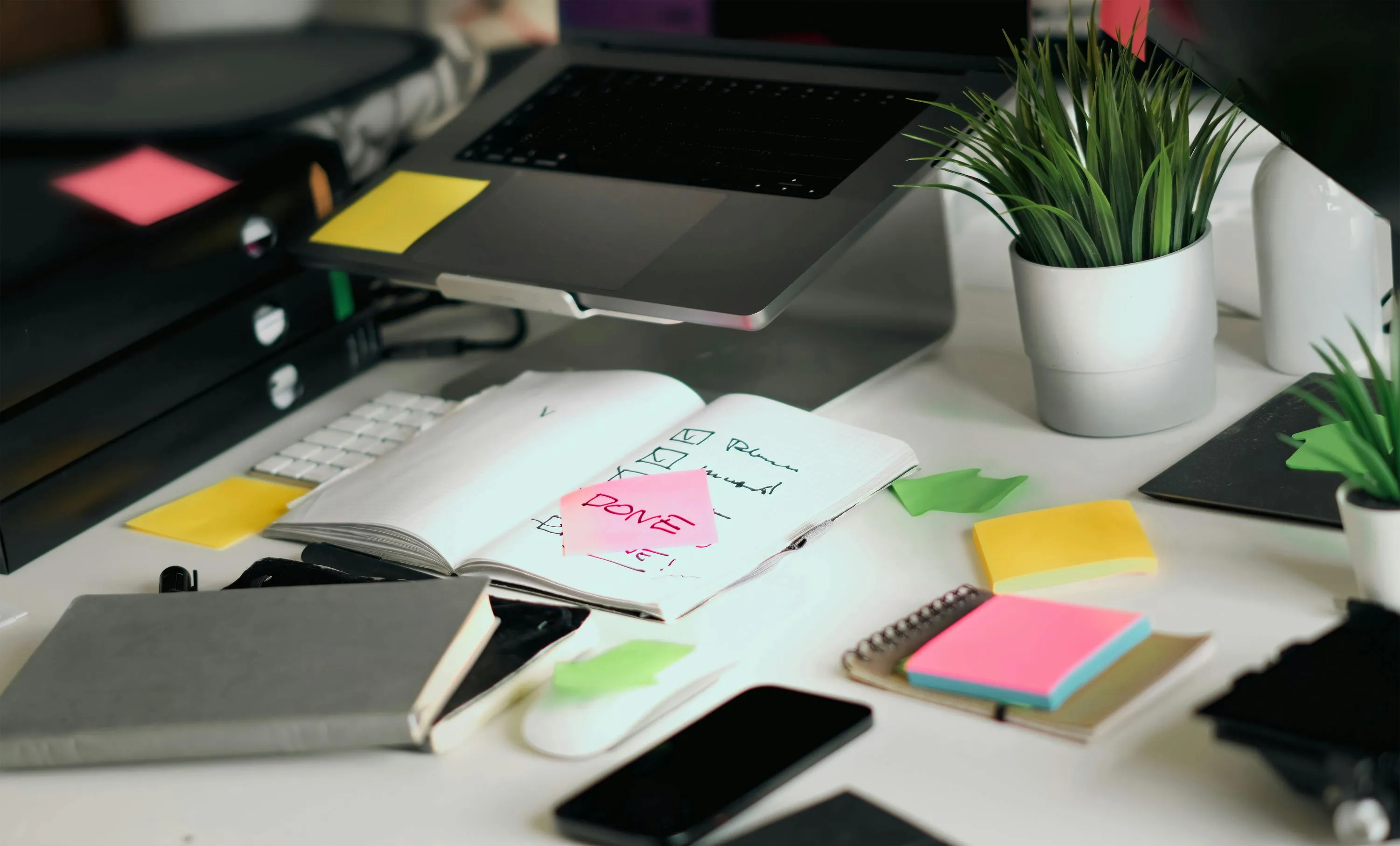 A messy desk with a laptop, notebook, and sticky notes, representing a self-sabotage pattern or strategy.