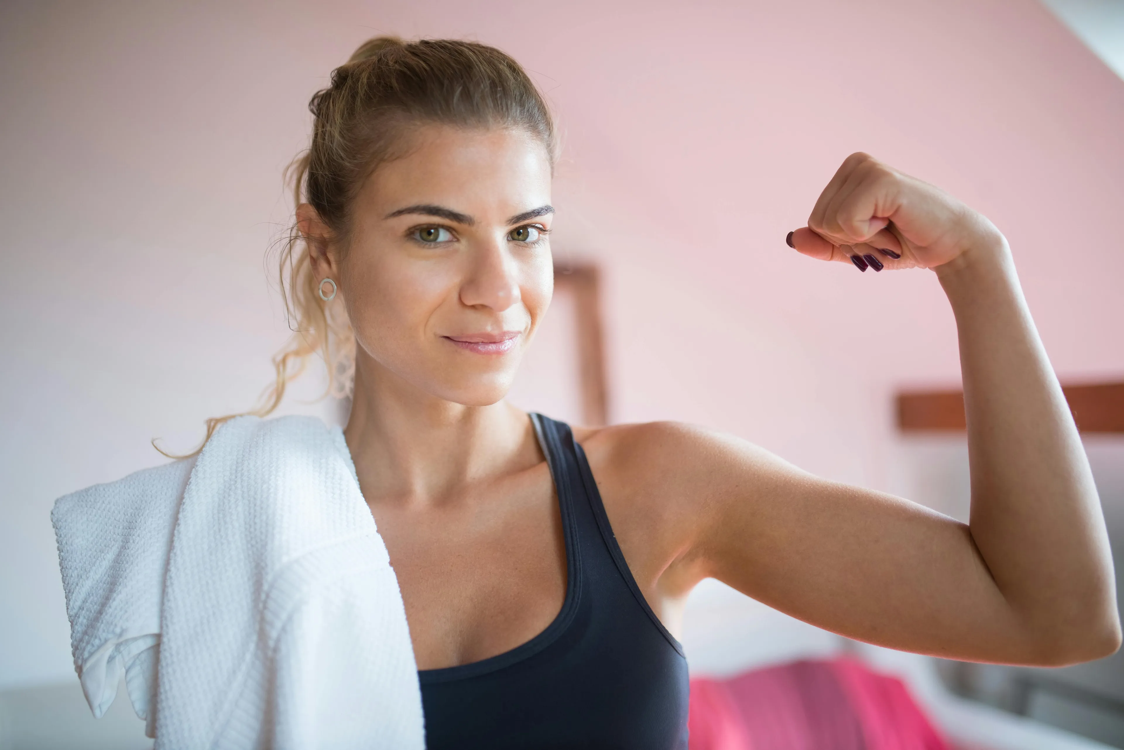 A fit woman, towel over shoulder, flexing arm. Ready for a power-up to avoid self-sabotage on Monday morning.
