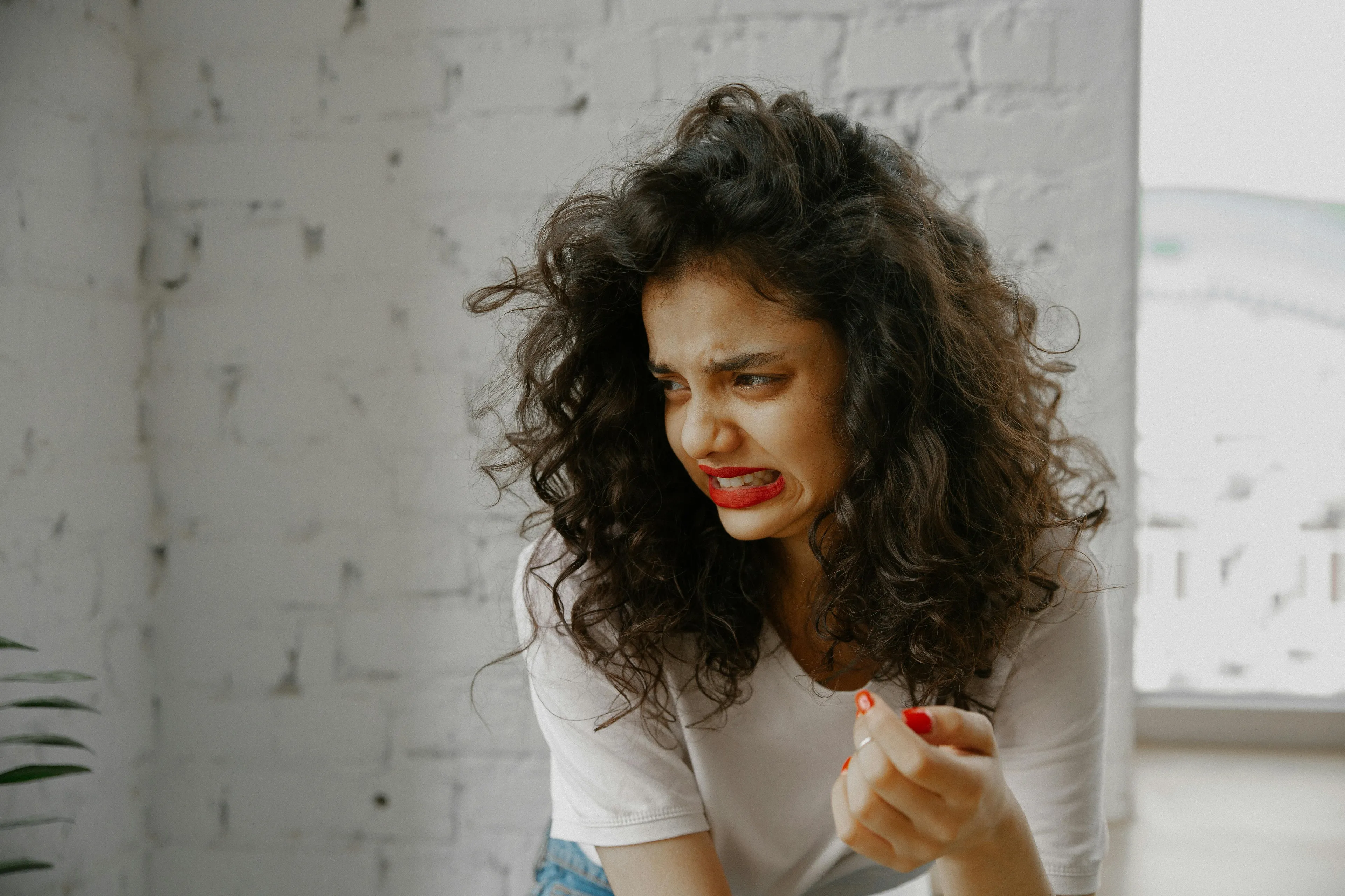 A young woman with curly hair makes a distressed face, thinking about her self-sabotage pattern.