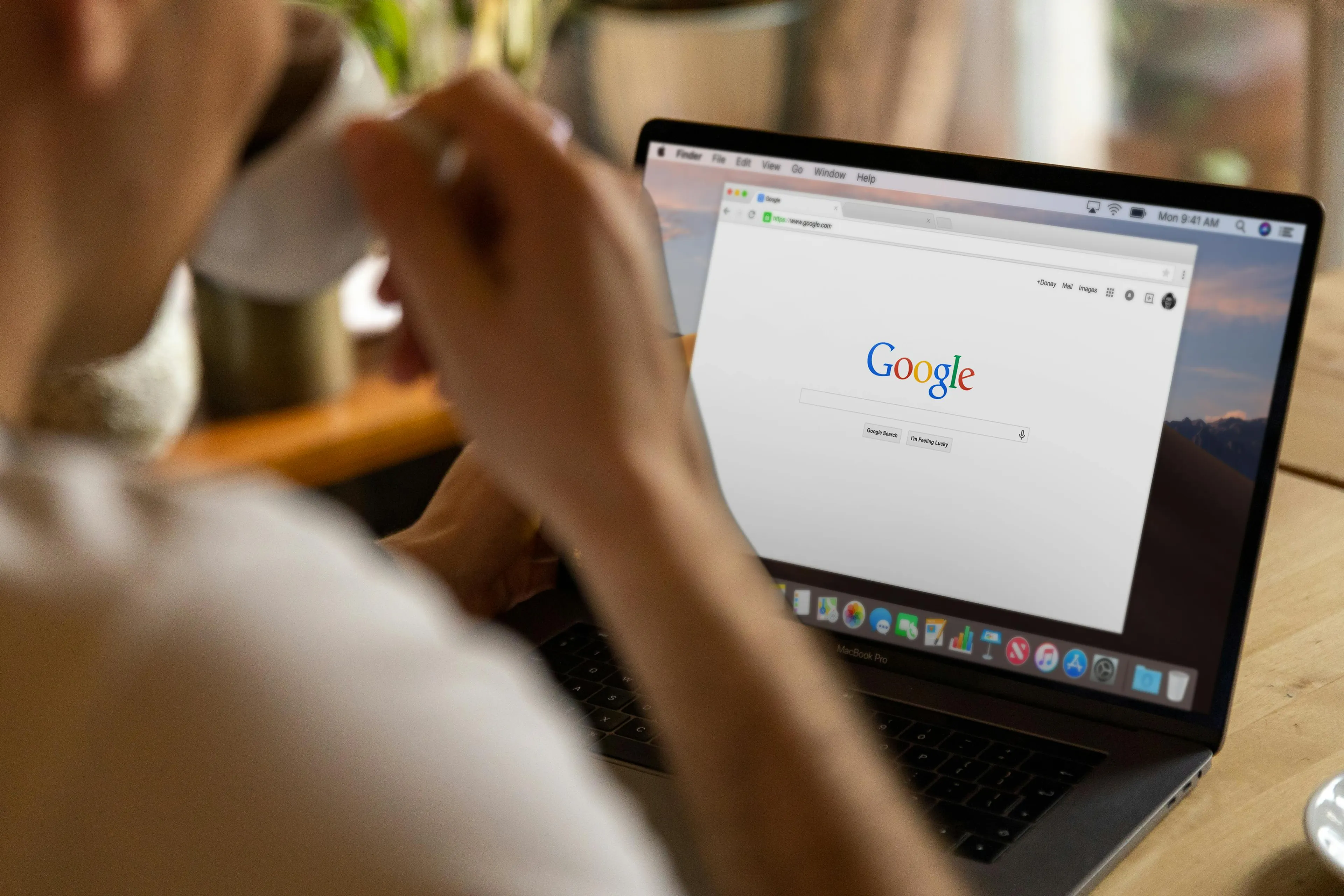 A person sips coffee while looking at a laptop with multiple browser tabs open, representing a self-sabotage pattern.