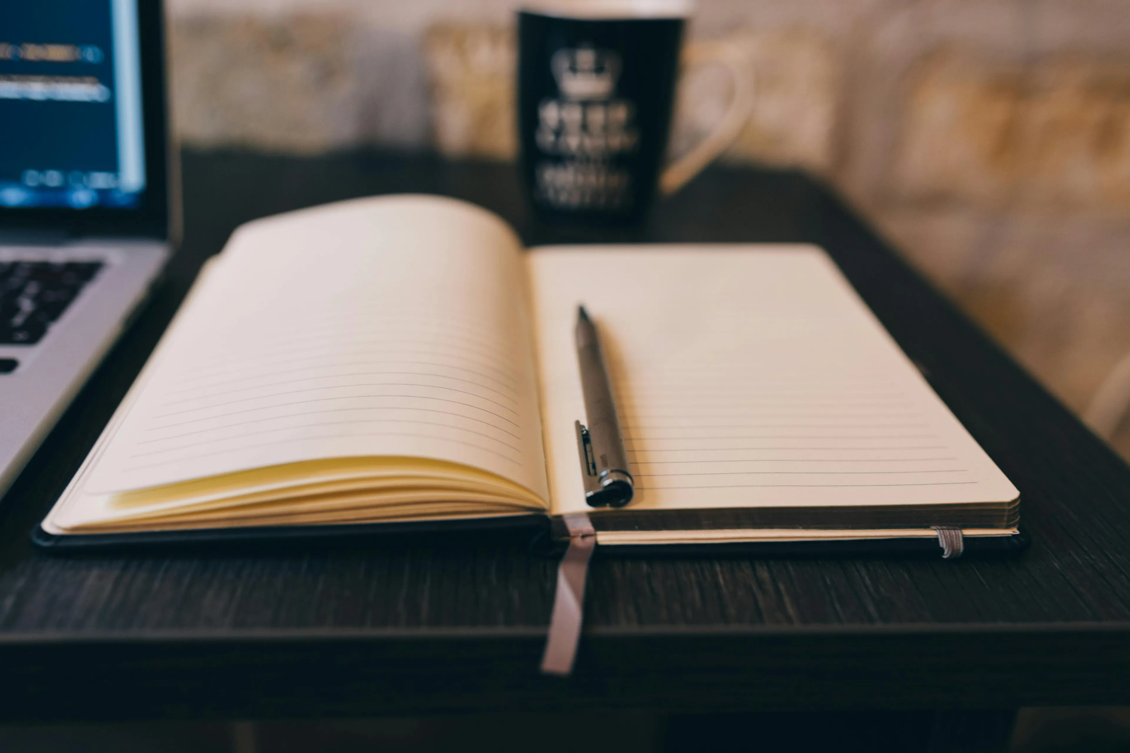 An open, blank journal with a pen, next to a laptop and mug. Ready to explore your self-sabotage pattern.