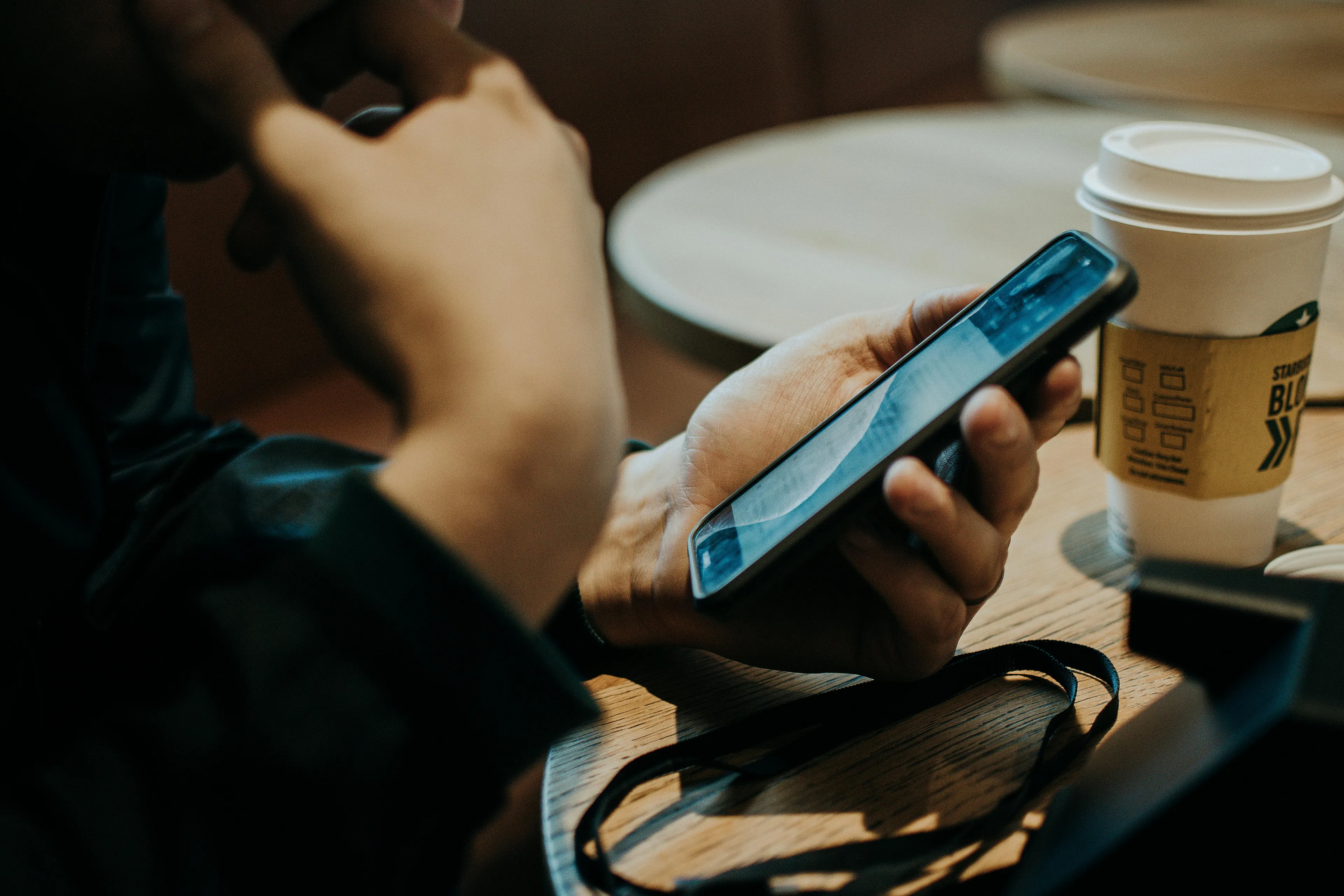 A person holds a phone, contemplating a social post typo. What's your self-sabotage pattern? Coffee sits nearby.