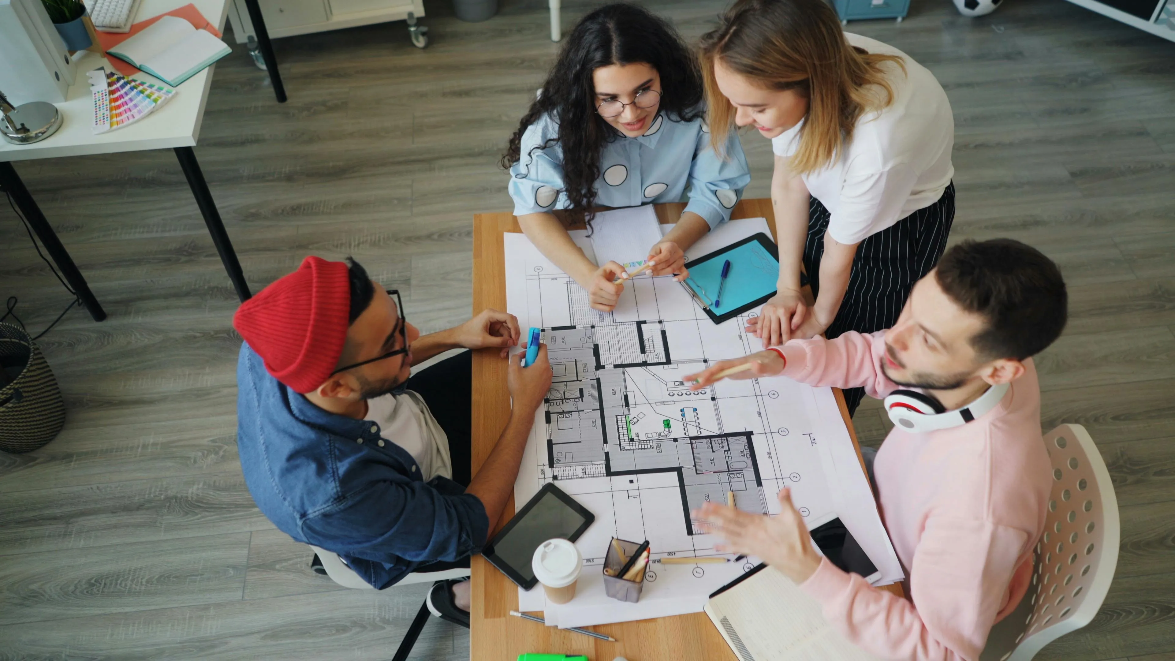 Four young professionals collaborating on architectural blueprints, showing a signature move in a group project.