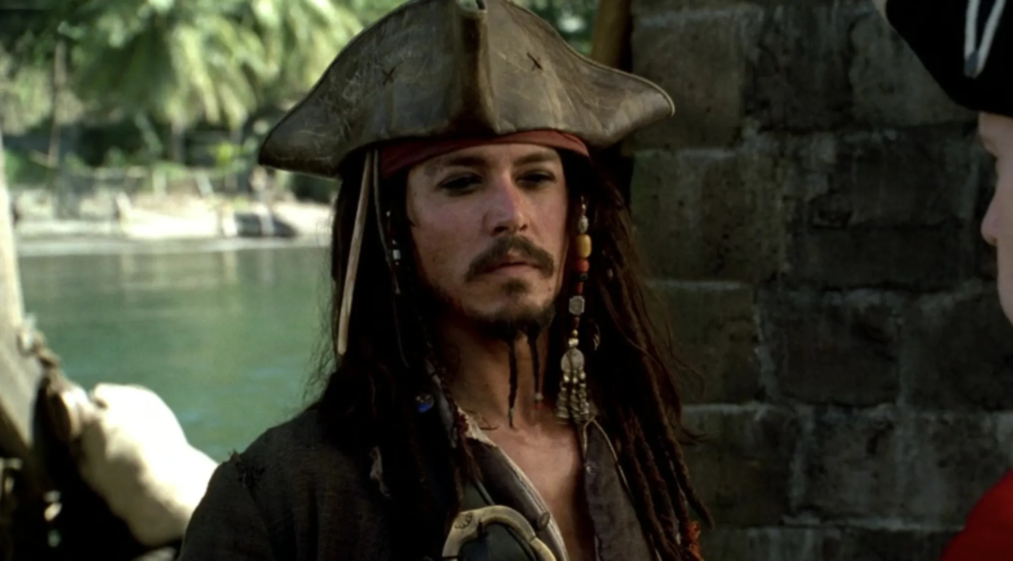 Captain Jack Sparrow with his signature dreadlocks, goatee, and tricorn hat, looking left. He is the character of this captain.