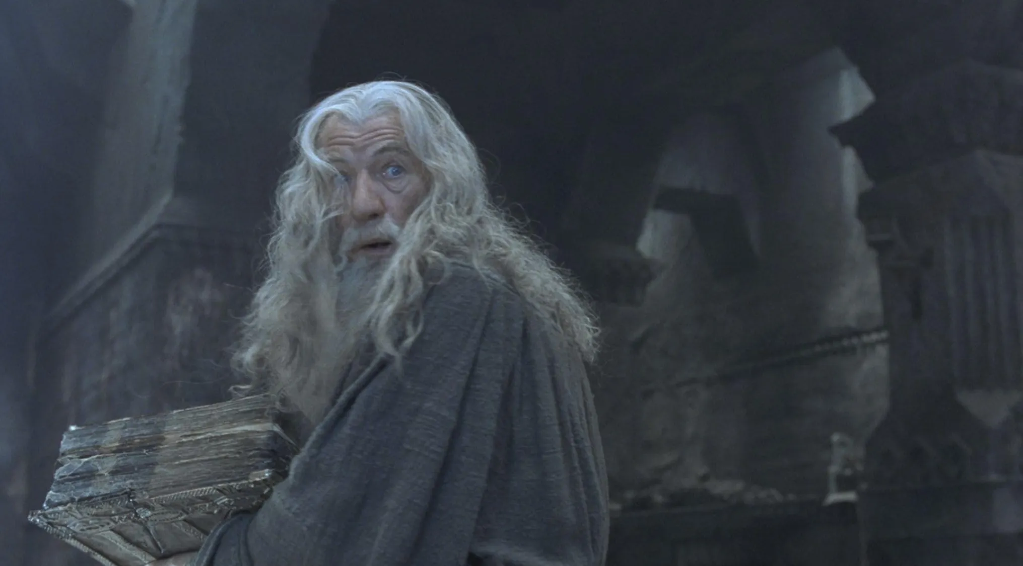 Old wizard with long white hair and beard, wearing a grey robe and holding a large book. Name the character.