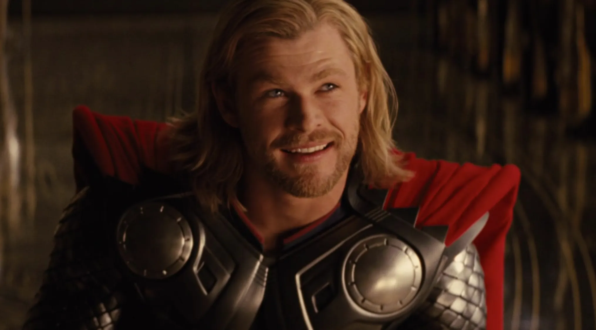 Name the character: Chris Hemsworth as Thor, smiling, with blonde hair, beard, and wearing his superhero armor with a red cape.